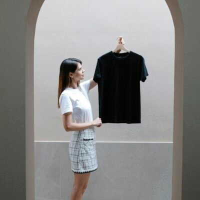 Side view full body of trendy young female designer in mini skirt and boots standing at arched doorway and demonstrating black t shirt